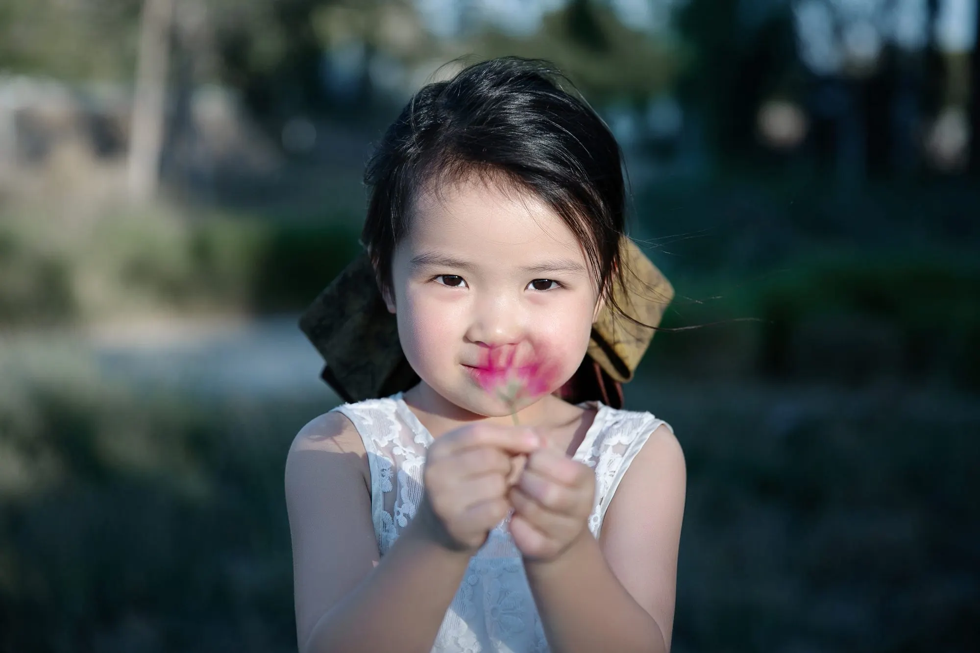 Little girl holding a pink blossom at golden hour, frame 5 of 10
